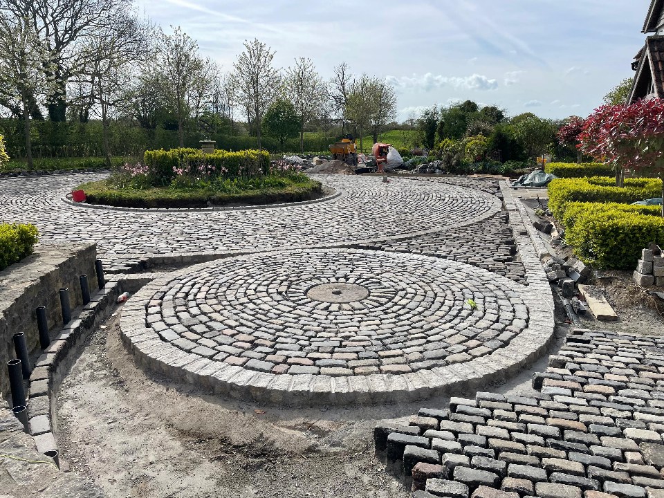 Hand-laid granite cobble setts in concentric circles with a curved retaining wall
