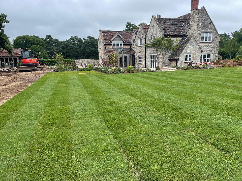 A neatly striped, freshly turfed lawn in front of a large stone home