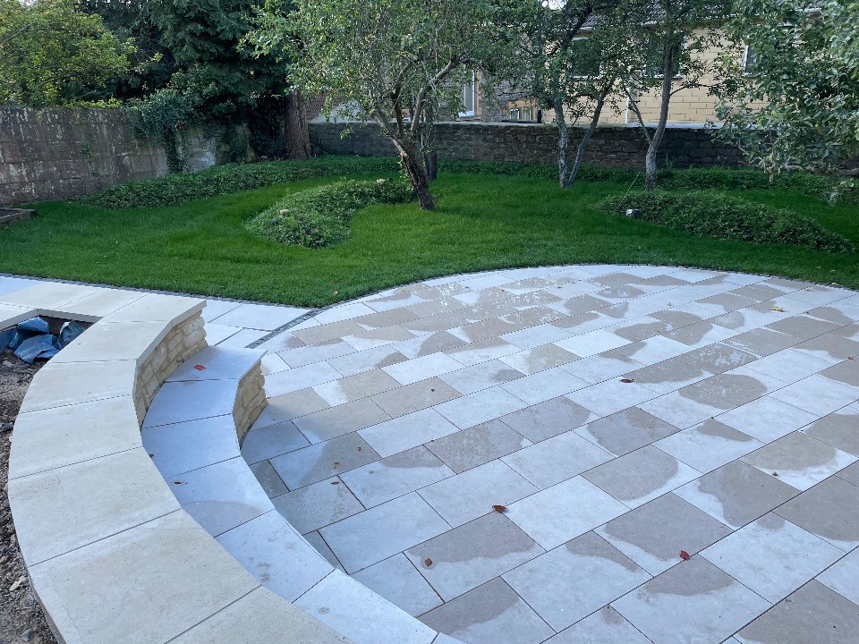 Curved Bath-stone patio with a low retaining wall and lawn beyond