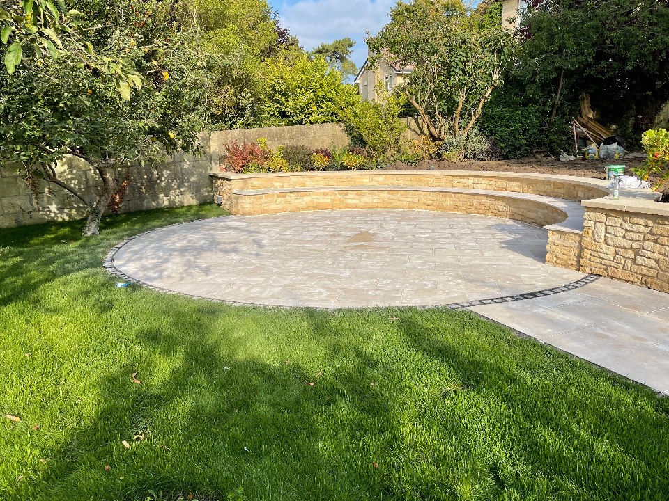 Circular natural-stone patio set into a lawn with a curved retaining wall