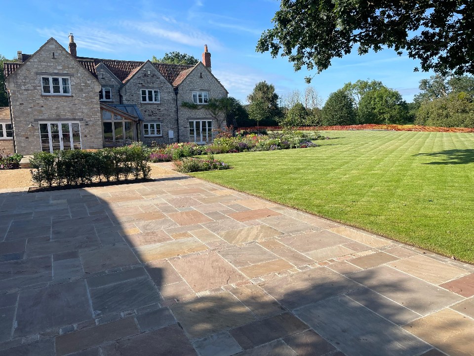 Indian-sandstone patio leading to a manicured lawn beside a stone home