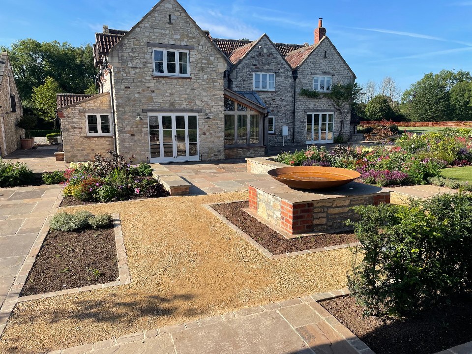 A sandstone courtyard garden with a copper fire bowl and gravel planting beds