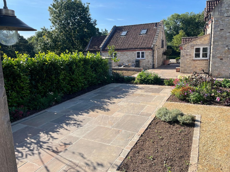 A sandstone patio framed by clipped hedging and planted borders