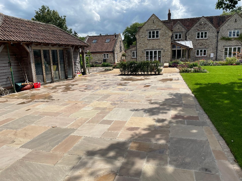 A large sandstone courtyard between a timber barn, a stone home and a lawn