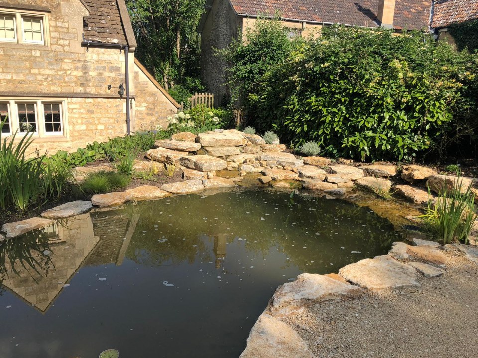 A natural wildlife pond edged with local stone beside a cottage